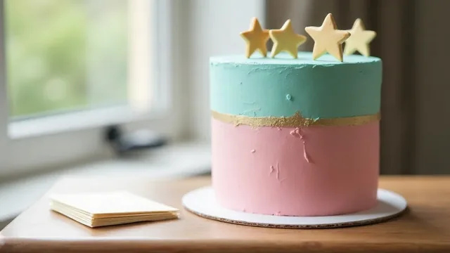 A tall round cake, pink below and teal above with a gold band and sugar stars on top, next to a small stack of blank cards